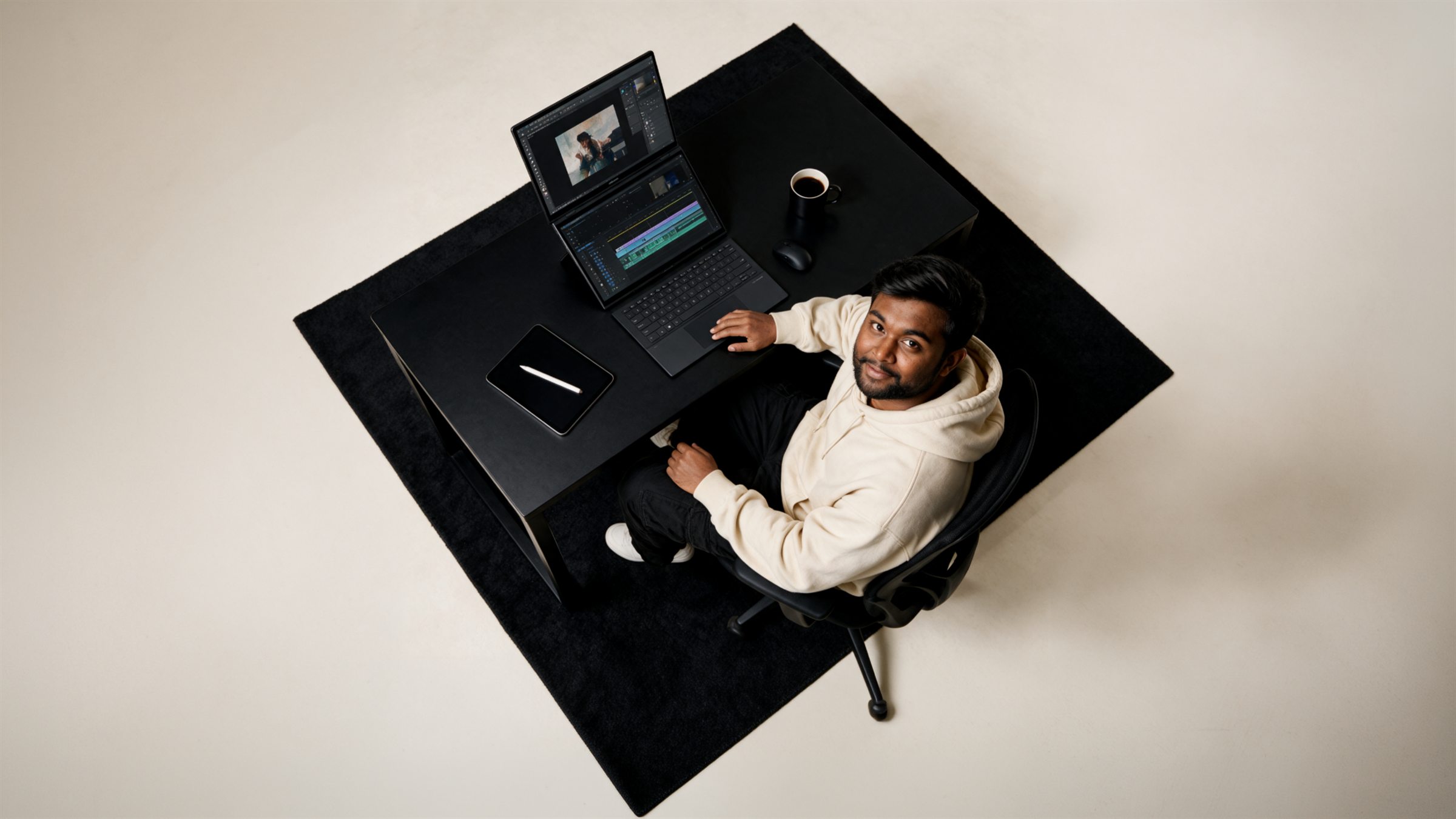 Vishnu Nakkella seen from directly above, seated at a black desk editing video on a dual-screen laptop